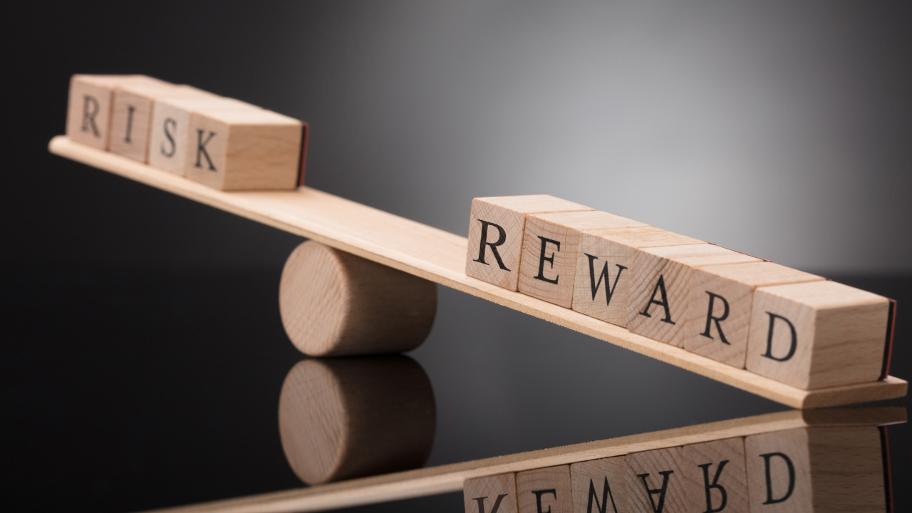 Wooden seesaw balancing blocks labeled RISK and REWARD, illustrating the concept of the risk-reward ratio in trading.