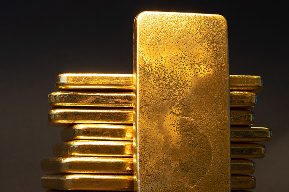Stack of shiny gold bars with a large gold bullion in the foreground, illustrating the question: will gold climb higher in 2025?