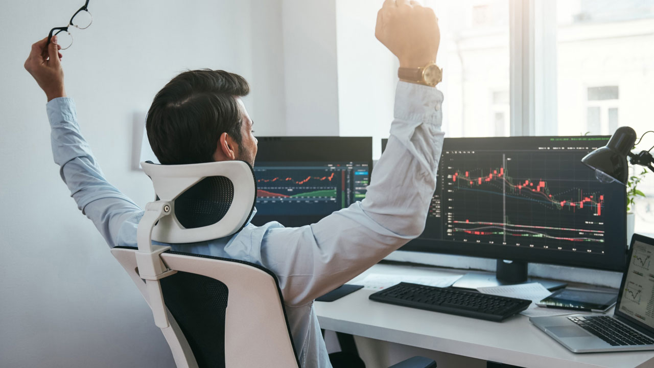 A forex trader celebrating a successful trade in front of multiple monitors displaying market charts, symbolizing the rewards of discipline and patience in trading.