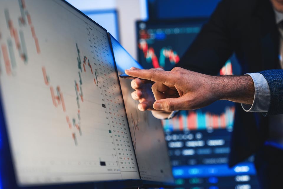 A close-up of a hand pointing at a computer monitor displaying technical trading charts, illustrating technical trading strategies for day traders