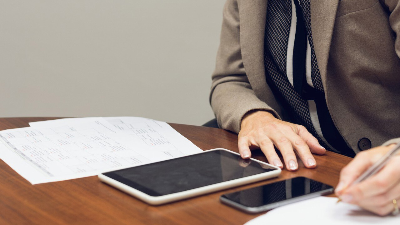 A professional trader taking notes with a tablet and printed trading journal on a desk, representing the process of creating a crypto trading journal.