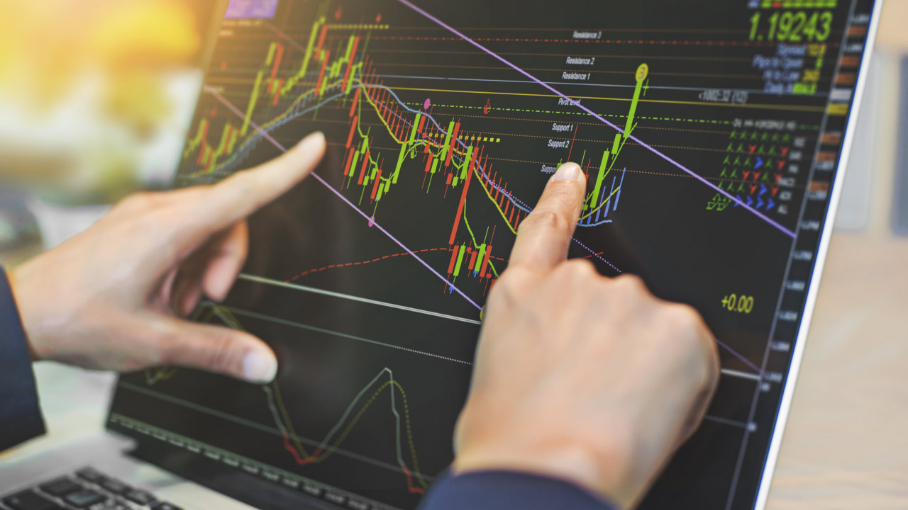 Two hands pointing at a laptop screen displaying a complex financial chart with lines, candles, and numbers, illustrating 5 signs that indicate it’s time to change your trading strategy