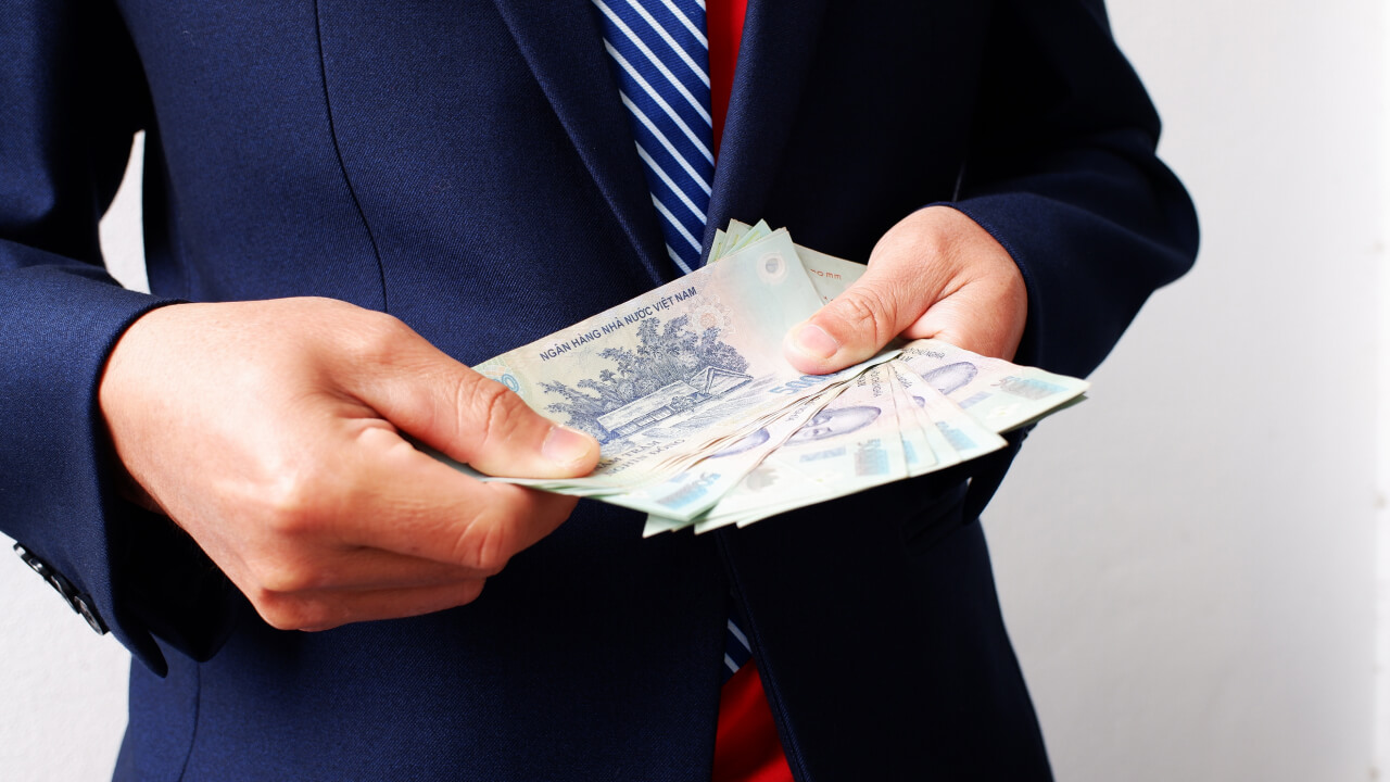  a person wearing a dark blue suit and striped tie is holding and counting a stack of Vietnamese đồng banknotes