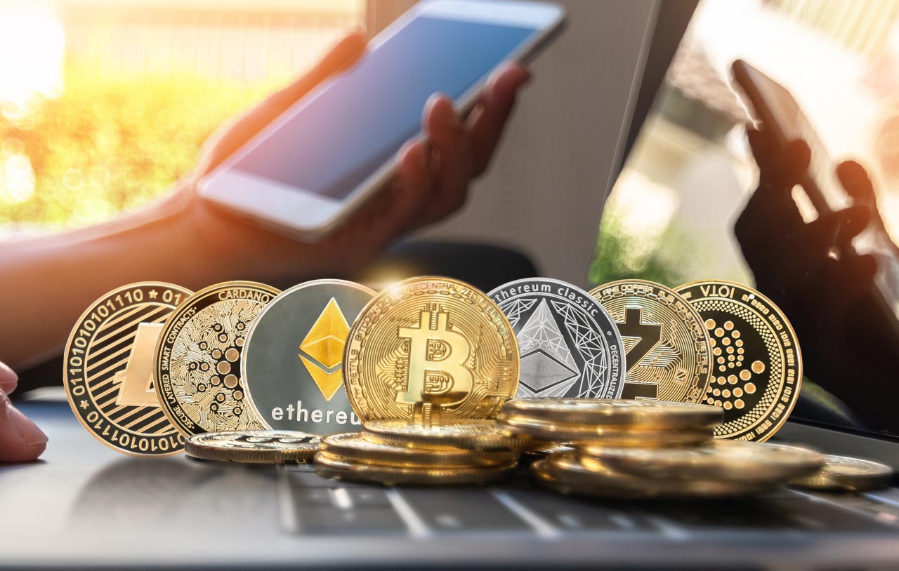 various popular cryptocurrency coins, including Bitcoin, Ethereum, Litecoin, Cardano, and others, placed on a laptop keyboard