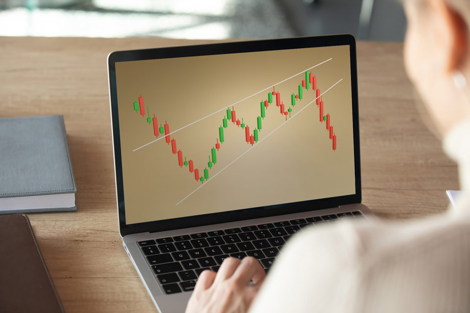 A person analyzing a trading chart on a laptop screen, displaying a wedge pattern with candlestick formations and trend lines.