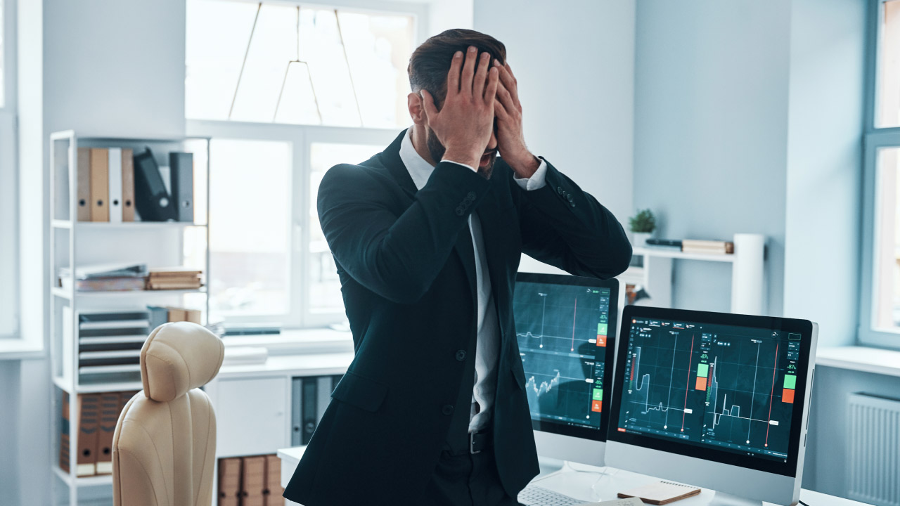 Reasons Why New Traders Give up Too Early, illustrated by a man in his trading room holding his face in frustration, surrounded by screens displaying forex charts and trading losses.