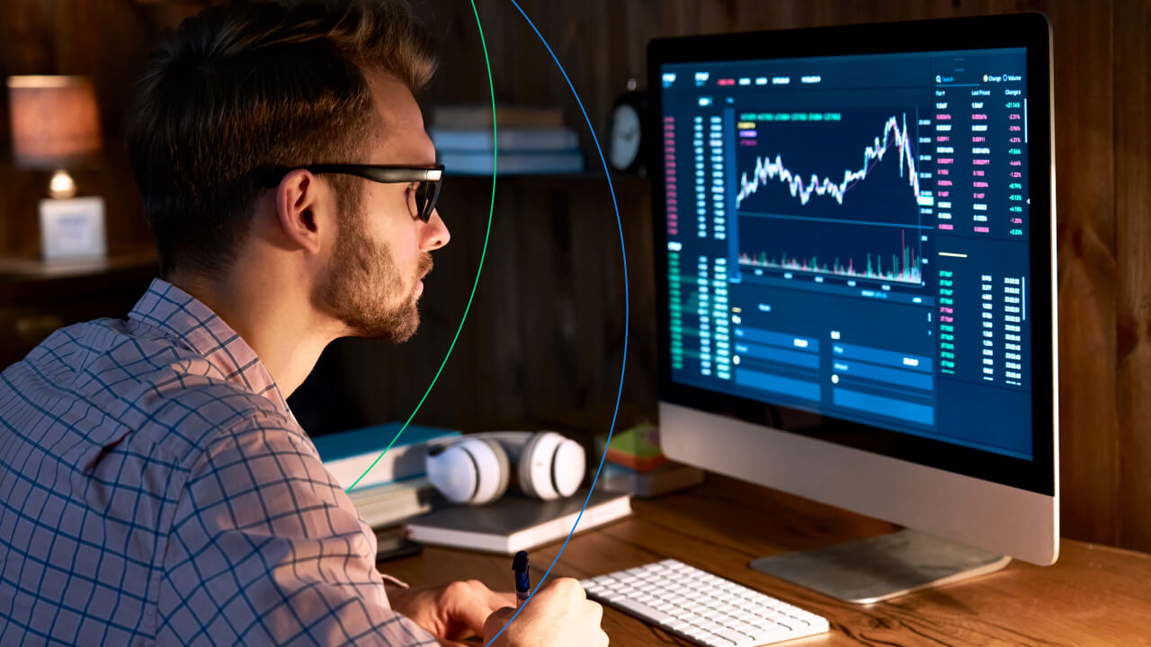 Top 5 Moving Average Trading Indicators, illustrated by a man wearing glasses analyzing financial charts on a large computer monitor in a home office setting.