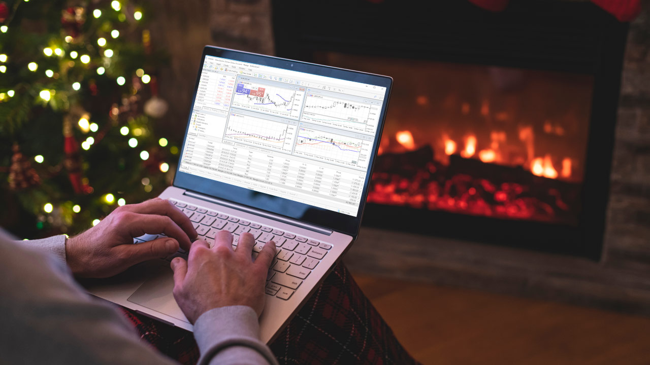Top Tips to Resume Trading After The 2023 Christmas Break, illustrated by a person trading forex on a laptop by a fireplace during Christmas, with trading charts displayed on the screen.