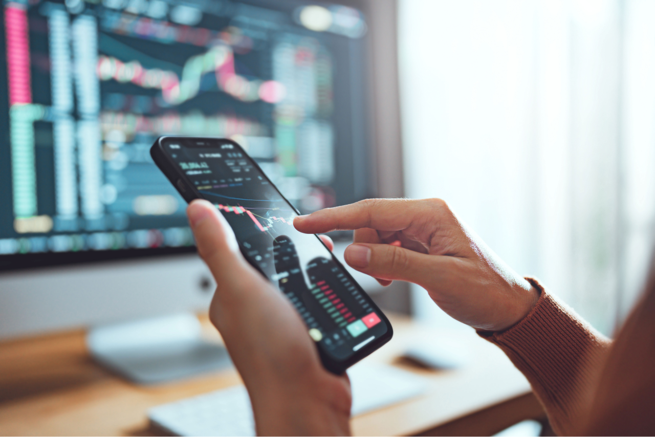 A trader monitoring forex charts on a smartphone and desktop screen, analyzing currency fluctuations to manage portfolio exposure effectively.