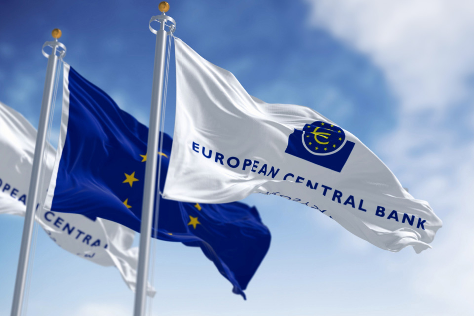 Flags of the European Central Bank (ECB) and the European Union waving against a blue sky. The ECB's rate decision significantly impacts forex markets and the Euro's value.