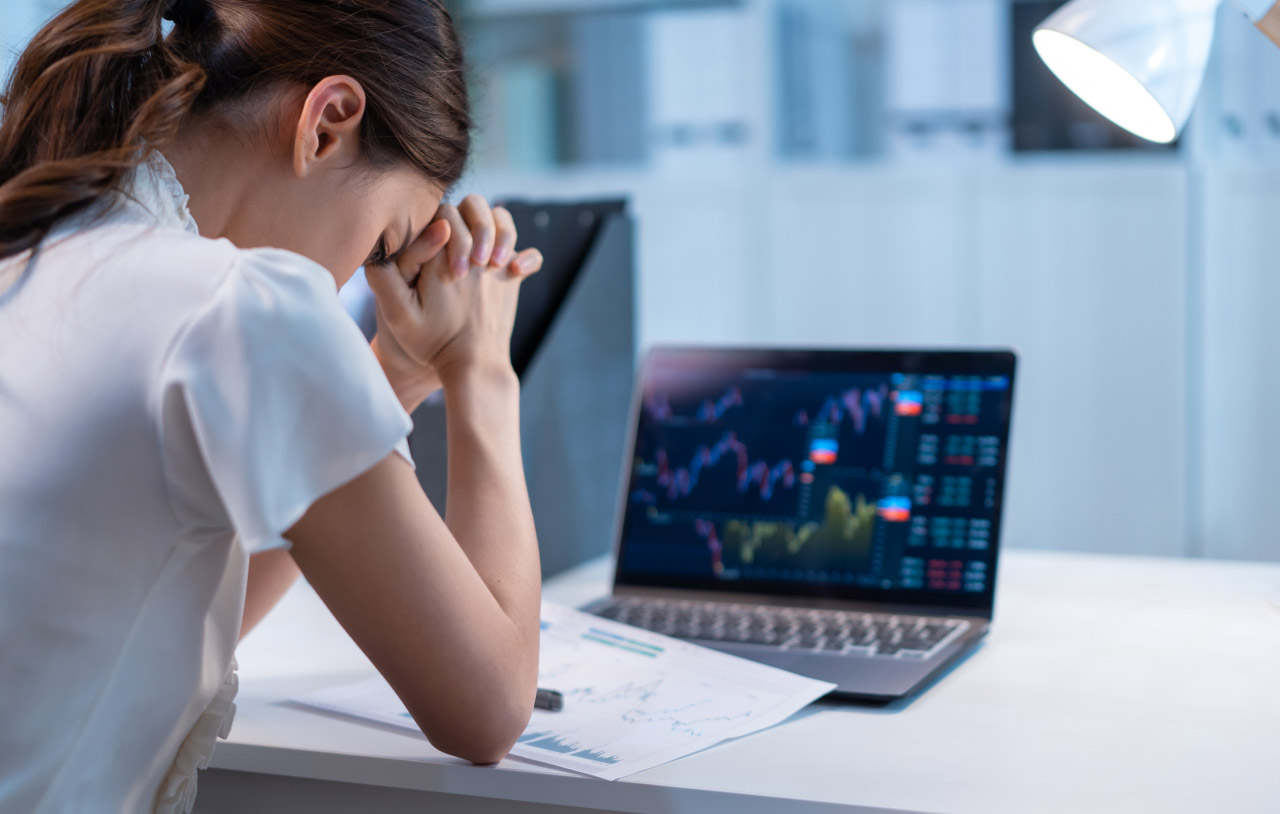 a woman sitting at a desk with her hands clasped and head bowed in frustration
