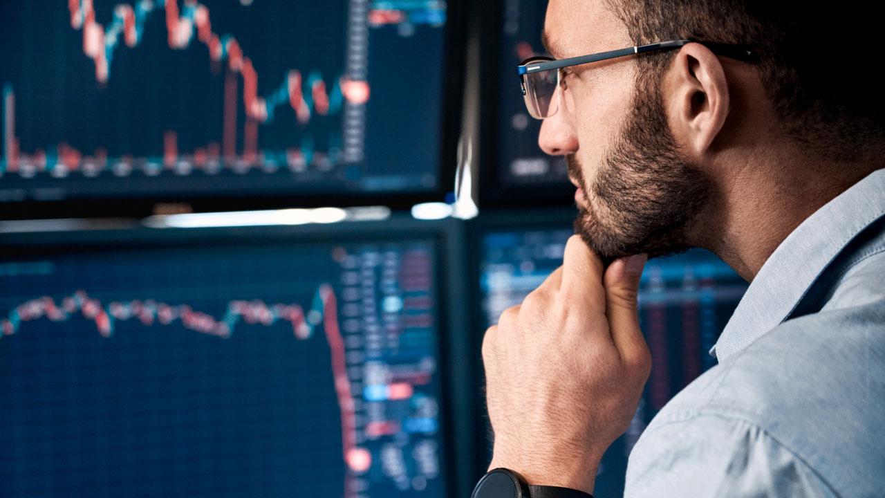 What is an Introducing Broker (IB)? A focused trader analyzes financial charts on multiple monitors, evaluating market movements and trading opportunities.