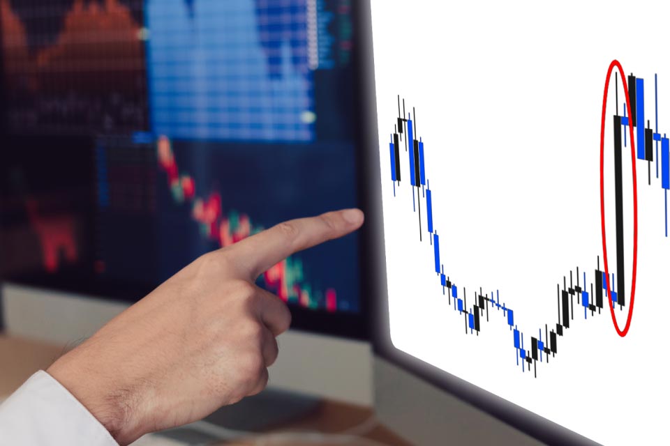 Close-up of a hand pointing at a candlestick chart on a computer screen, illustrating what wide ranging bars are
