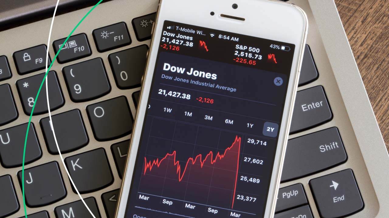 Index Trading Explained: How to Trade Indices – A smartphone displaying the Dow Jones Industrial Average chart placed on a laptop keyboard, symbolizing digital trading and market analysis.