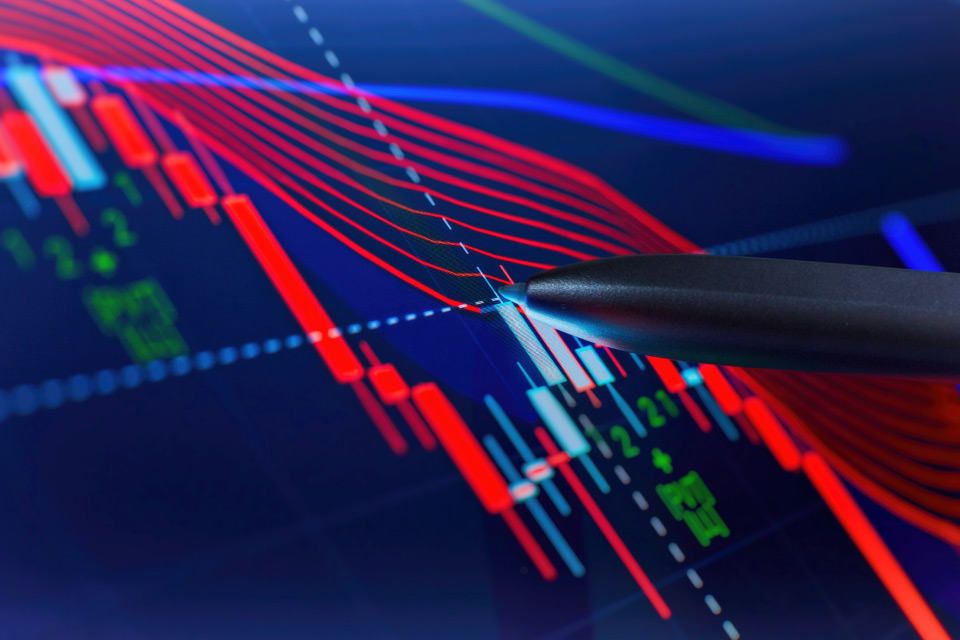 A close-up of a forex trading chart with red and blue indicators, showing a pen pointing at a candlestick, representing technical analysis and stochastic indicator usage in forex trading.