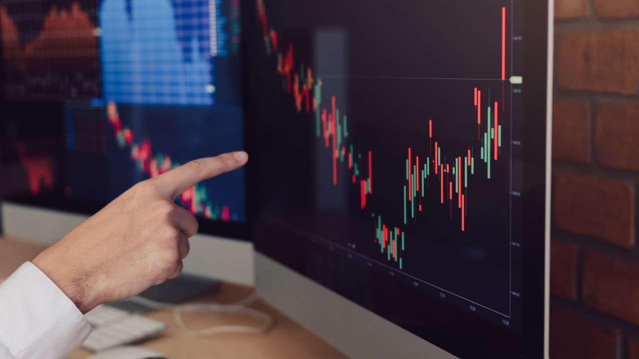 A person pointing at a computer screen displaying a candlestick chart, illustrating when to move from a demo to a live forex trading account.