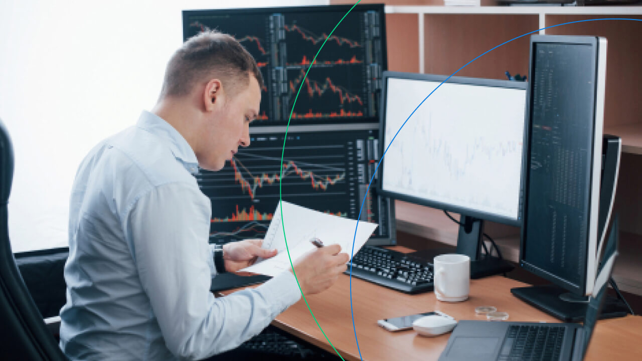 Forex Trading Strategies That Actually Work – A focused trader in a white shirt analyzes market charts and notes at a desk with multiple monitors displaying forex trading data, emphasizing the importance of strategic planning for successful trading.