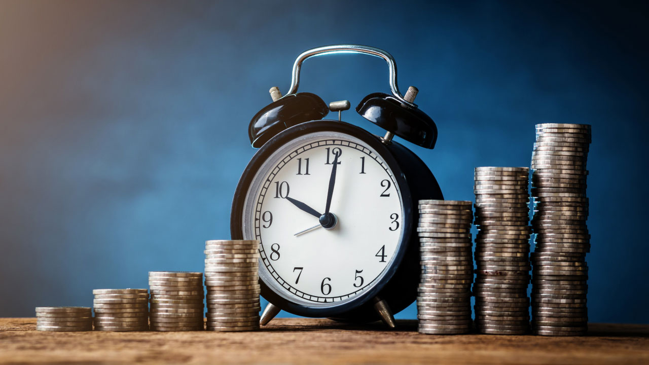 Black alarm clock surrounded by stacks of coins, symbolizing the connection between time and money.