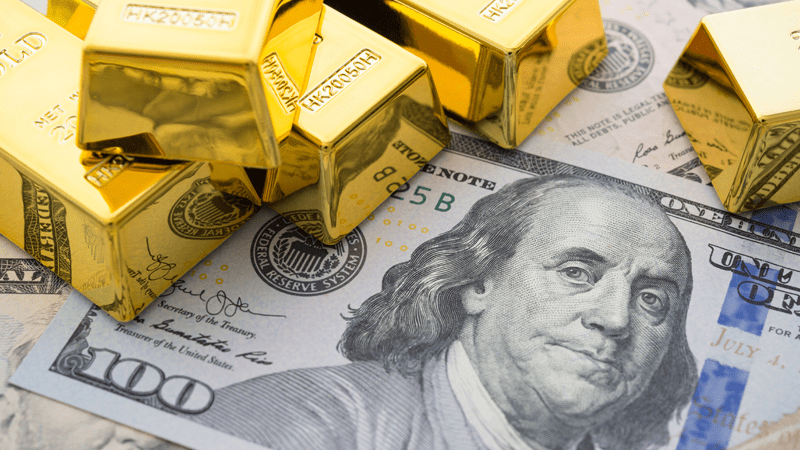 Stacks of gold bars placed on top of a U.S. 100-dollar bill featuring Benjamin Franklin