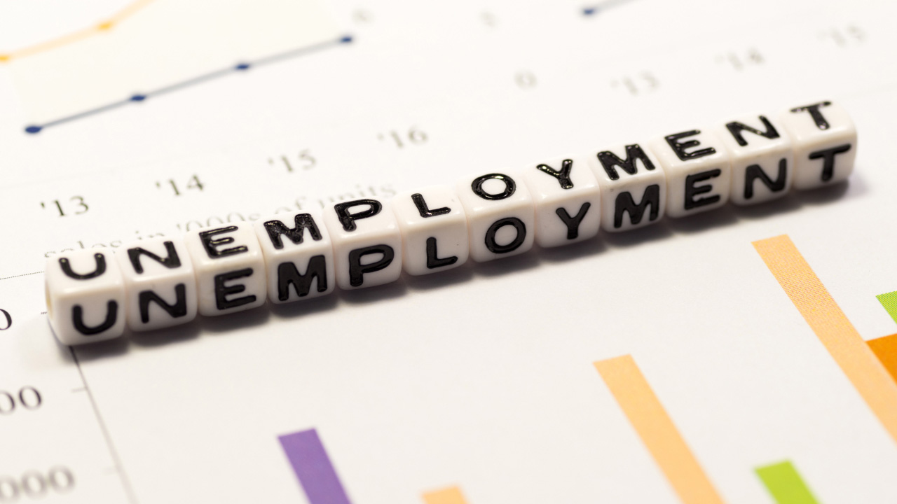 The image features the word "UNEMPLOYMENT" spelled out with white cube beads bearing bold black letters.