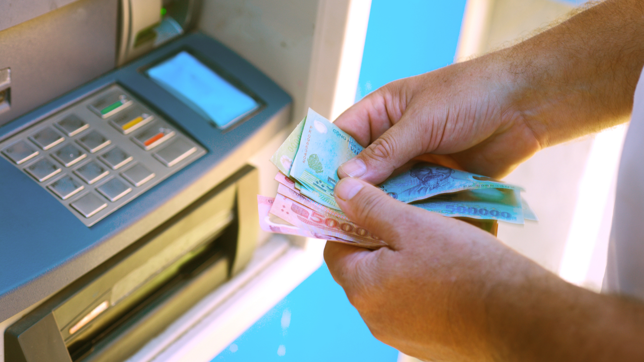 A person withdrawing and counting Vietnamese dong banknotes at an ATM, illustrating what traders need to know about fees when exchanging foreign currency to VND.