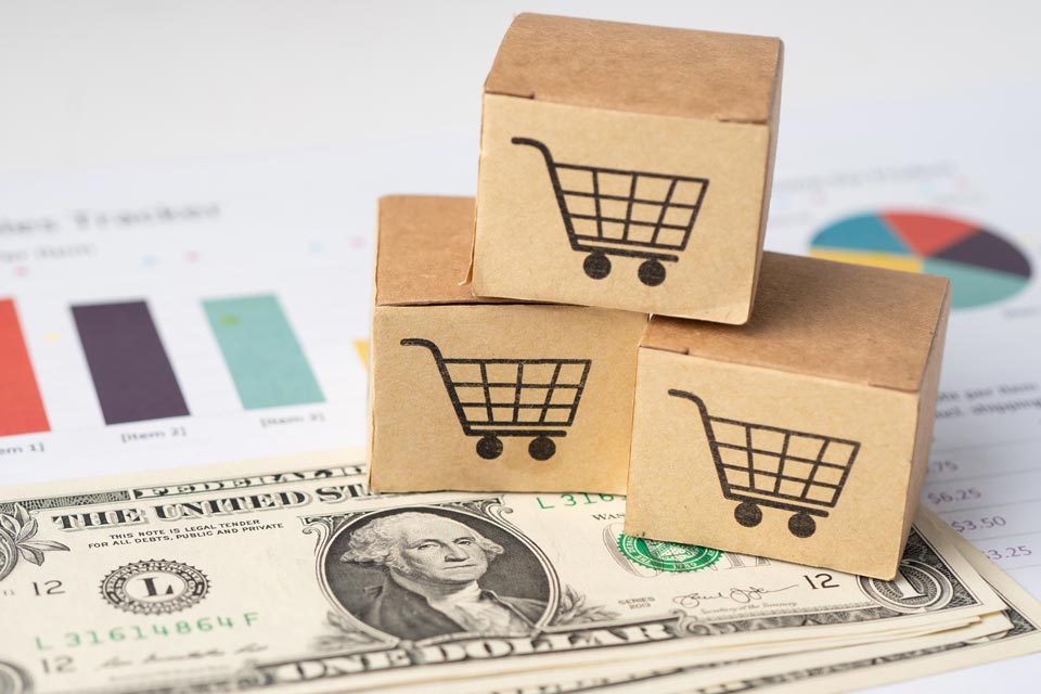 Stacked cardboard boxes with shopping cart icons placed on a US dollar bill