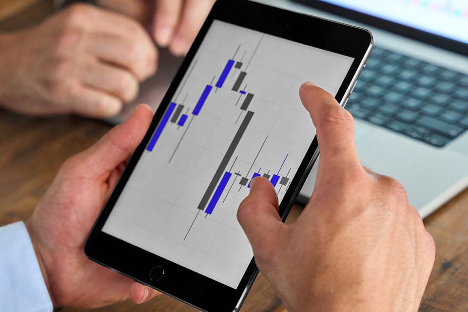 Hands holding a tablet displaying candlestick chart patterns, illustrating how to use the Inside Bar trading strategy in forex.