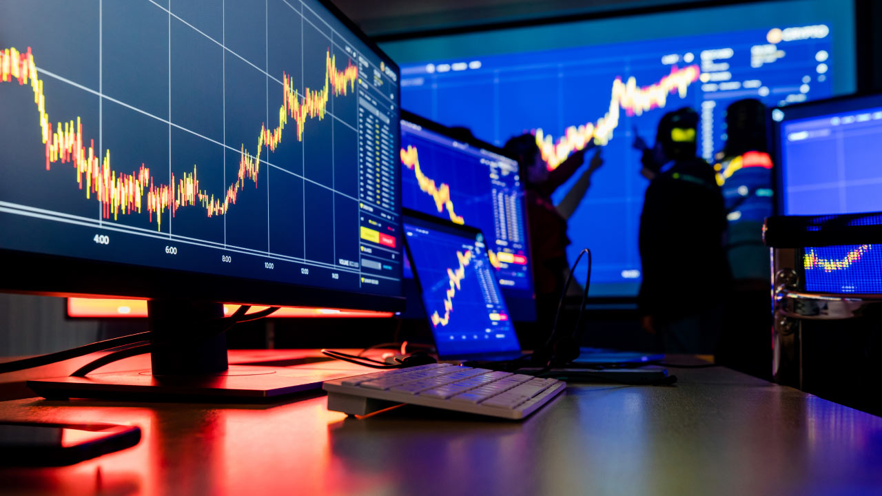 A modern trading setup with multiple monitors displaying various financial charts with candlestick patterns and trading data.