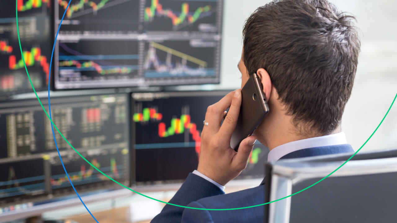 A trader in a suit talking on the phone while monitoring multiple financial charts, illustrating the concept of the Purchasing Manager's Index.