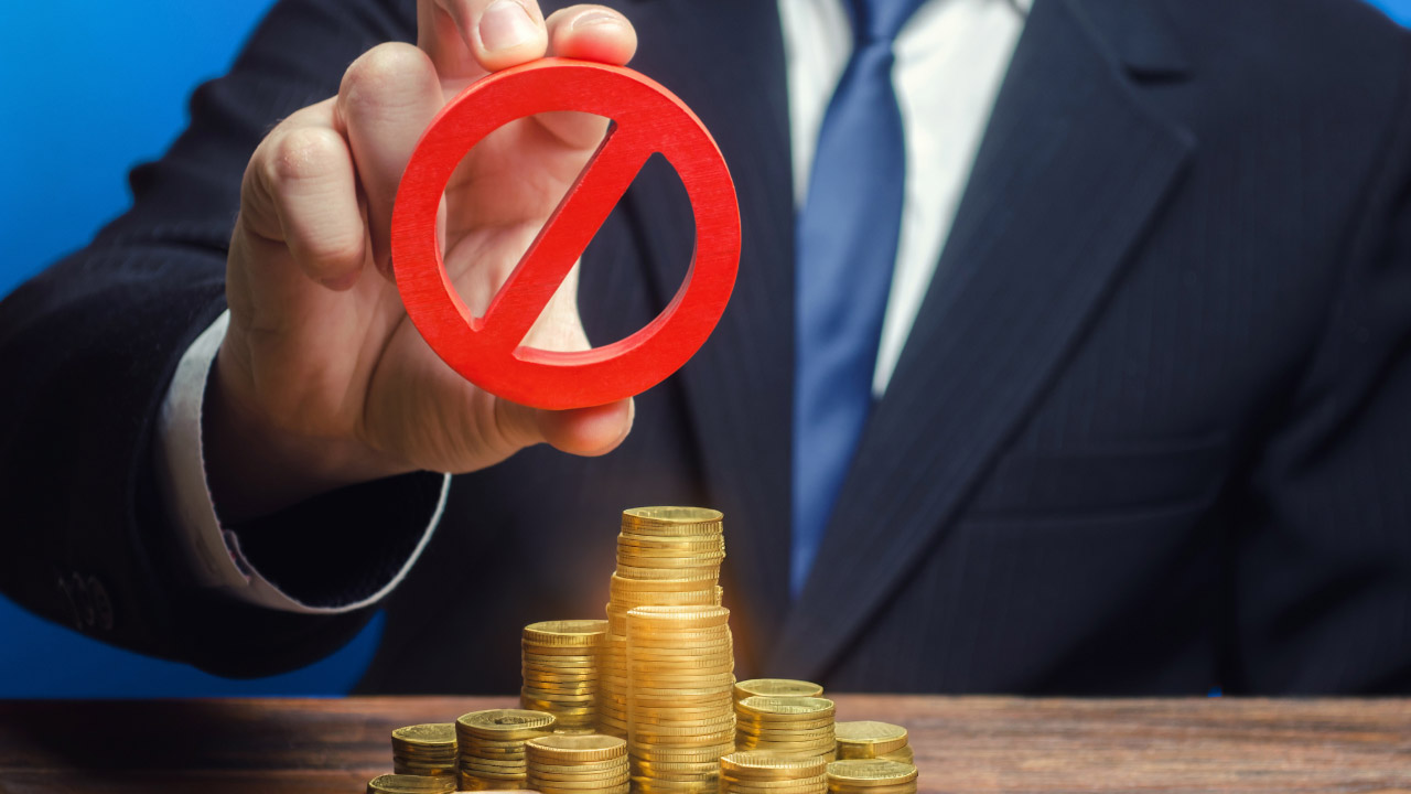 a man in a business suit holding a red prohibition symbol above a stack of gold coins