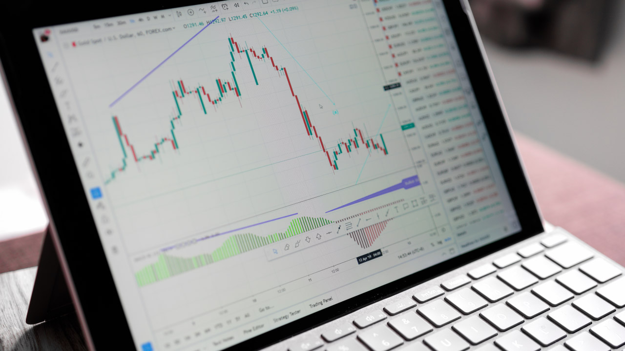 A close-up image of a tablet on a keyboard stand displaying a forex trading chart with candlestick patterns