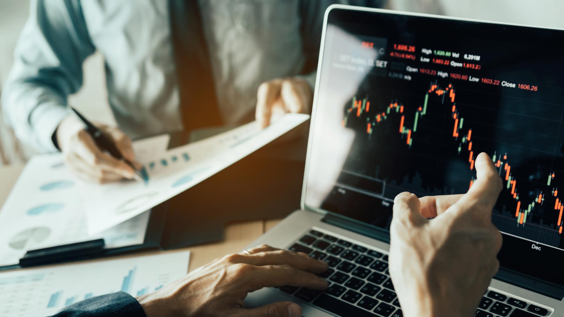 Online Trading vs Offline Trading: What's the Difference?, illustrated by two professionals analyzing financial charts on a laptop and document.