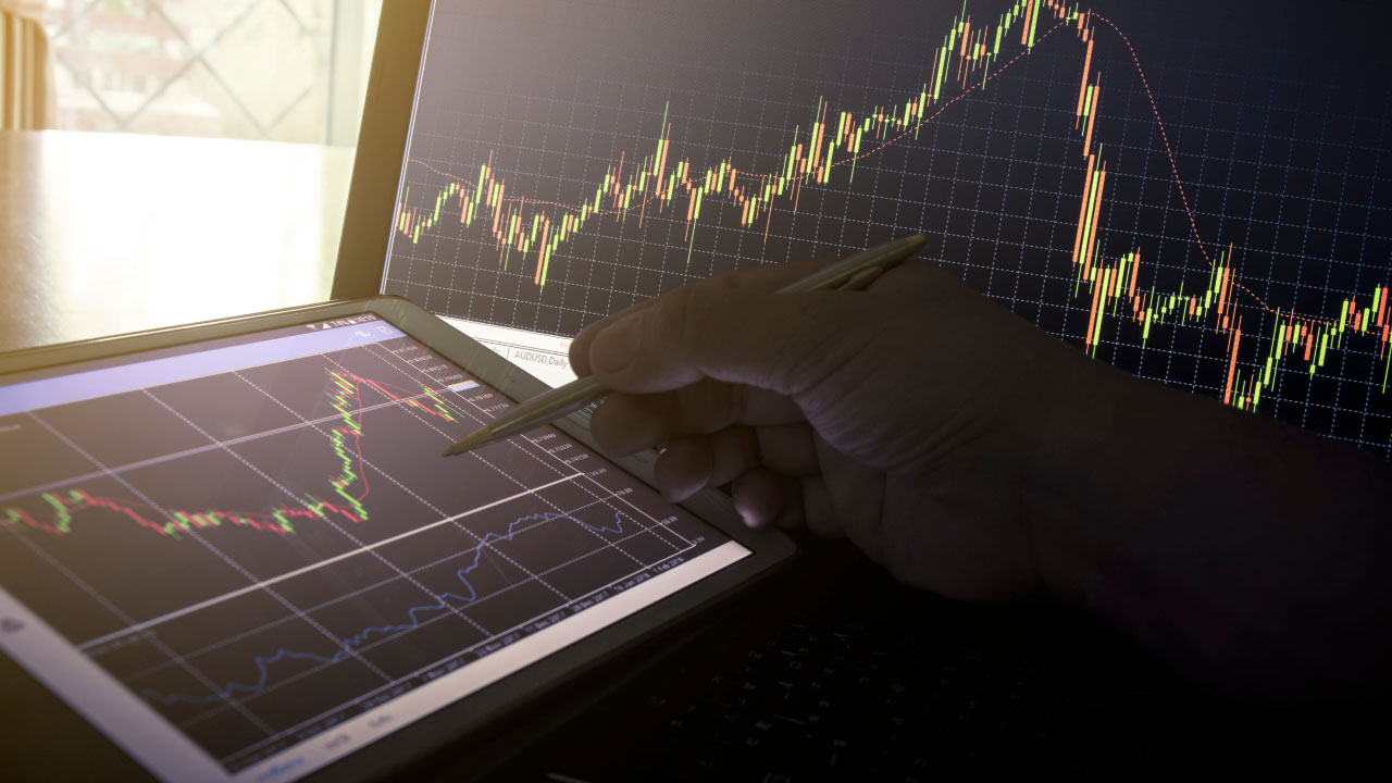 What is the Tick Volume Indicator? A trader analyzing candlestick charts on a tablet and laptop, highlighting market price movements and volume activity.