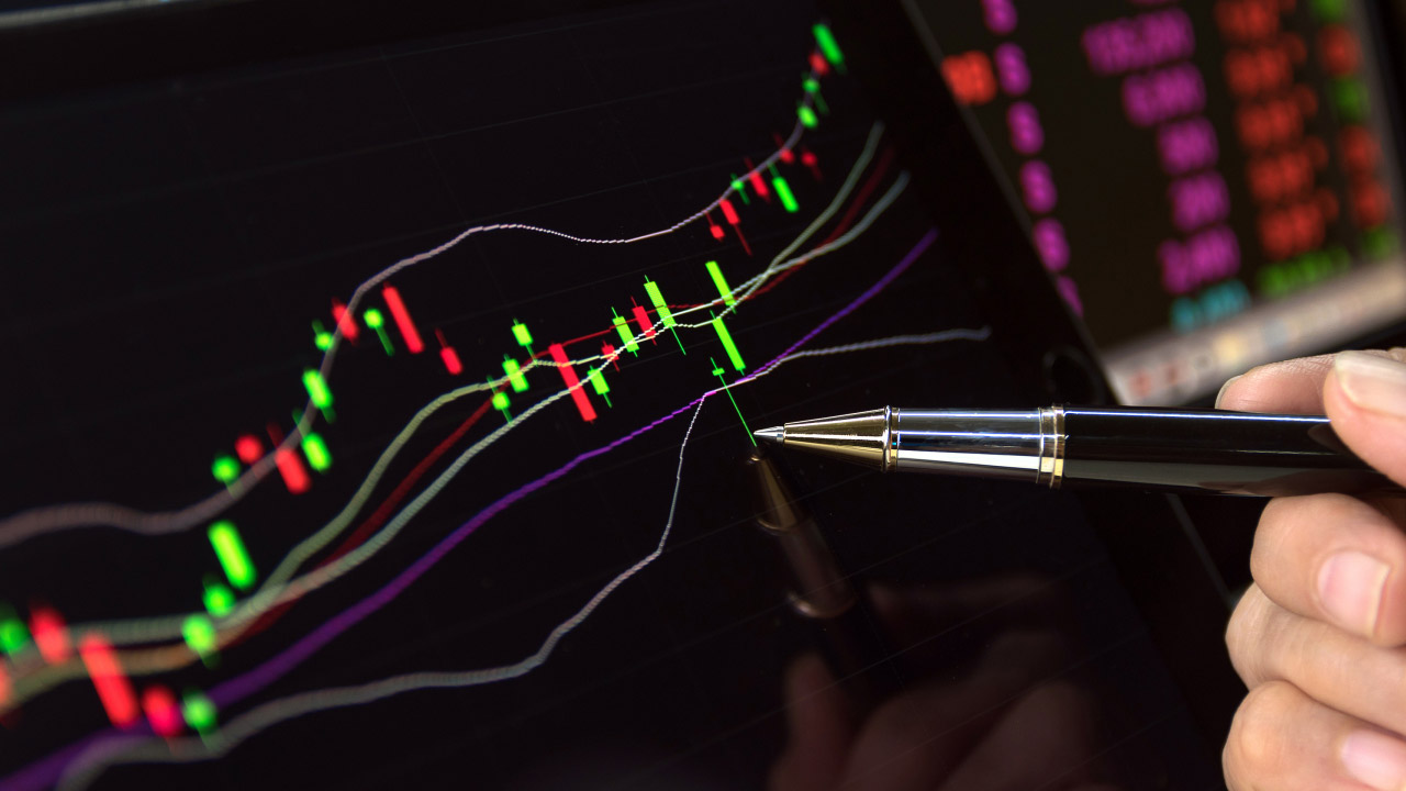 A close-up of a trader analyzing a candlestick chart with Bollinger Bands on a digital screen, using a pen to point at a specific price movement