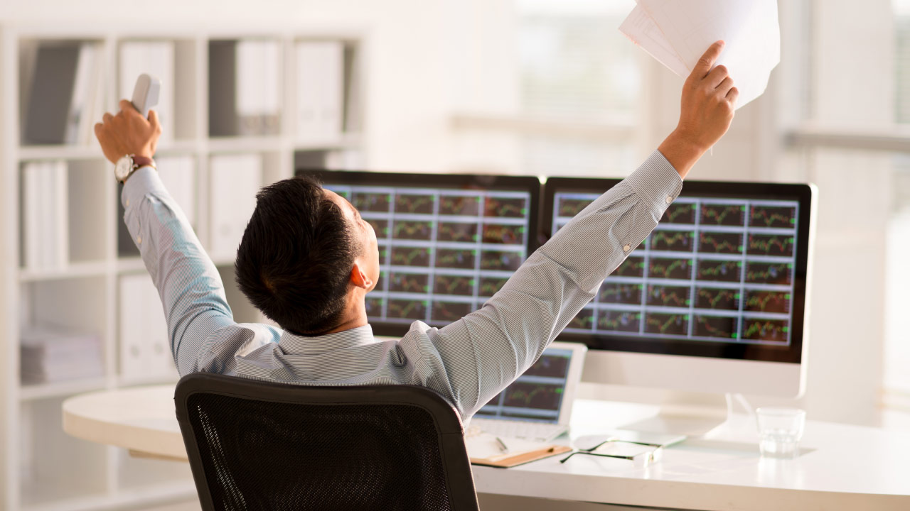 A man seated in an office chair raising his arms in celebration, illustrating the concept of what it takes to cultivate a winning attitude for forex trading.
