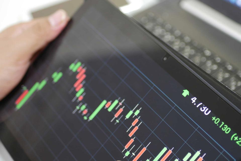 A trader holding a tablet displaying a candlestick chart with green and red bars, representing price movements in forex, illustrating the concept of "Breakout Trading and Fakeout Trading in Forex."