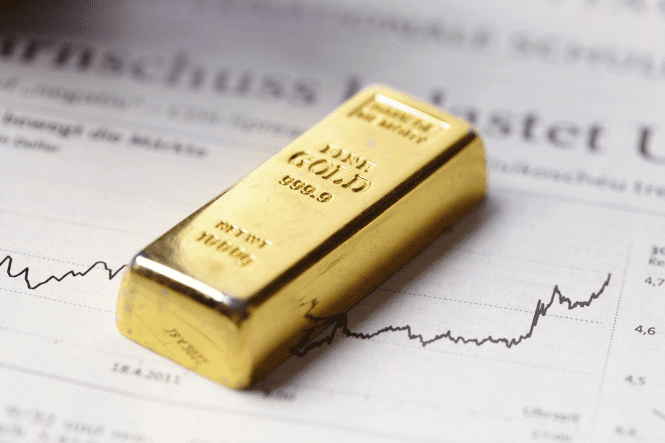 A gold bar labeled "999.9 FINE GOLD" lies on a financial newspaper displaying a rising price chart.