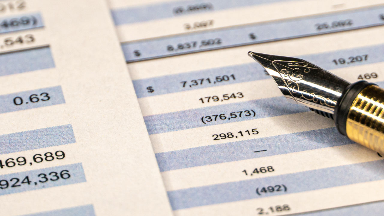 A close-up of a financial balance sheet with a fountain pen resting on it, illustrating how traders can analyze financial statements for informed trading decisions.