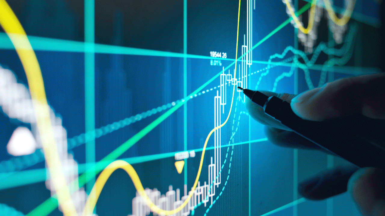 Hand holding a pen pointing at a digital financial chart with various technical indicators and candlestick patterns on a blue screen, illustrating the concept of the Nikkei 225.