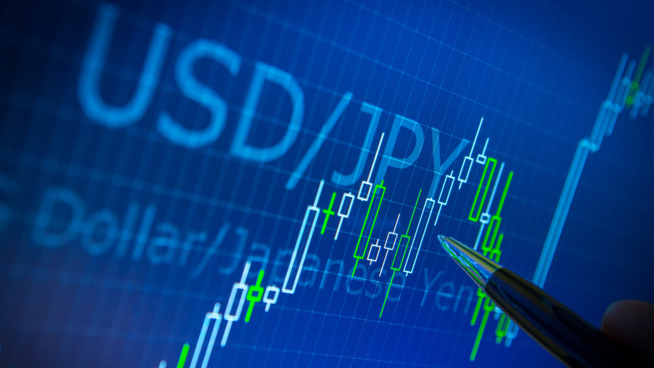A forex trading screen displaying the USD/JPY currency pair with candlestick chart analysis, showing market trends and a pen pointing at price movements.