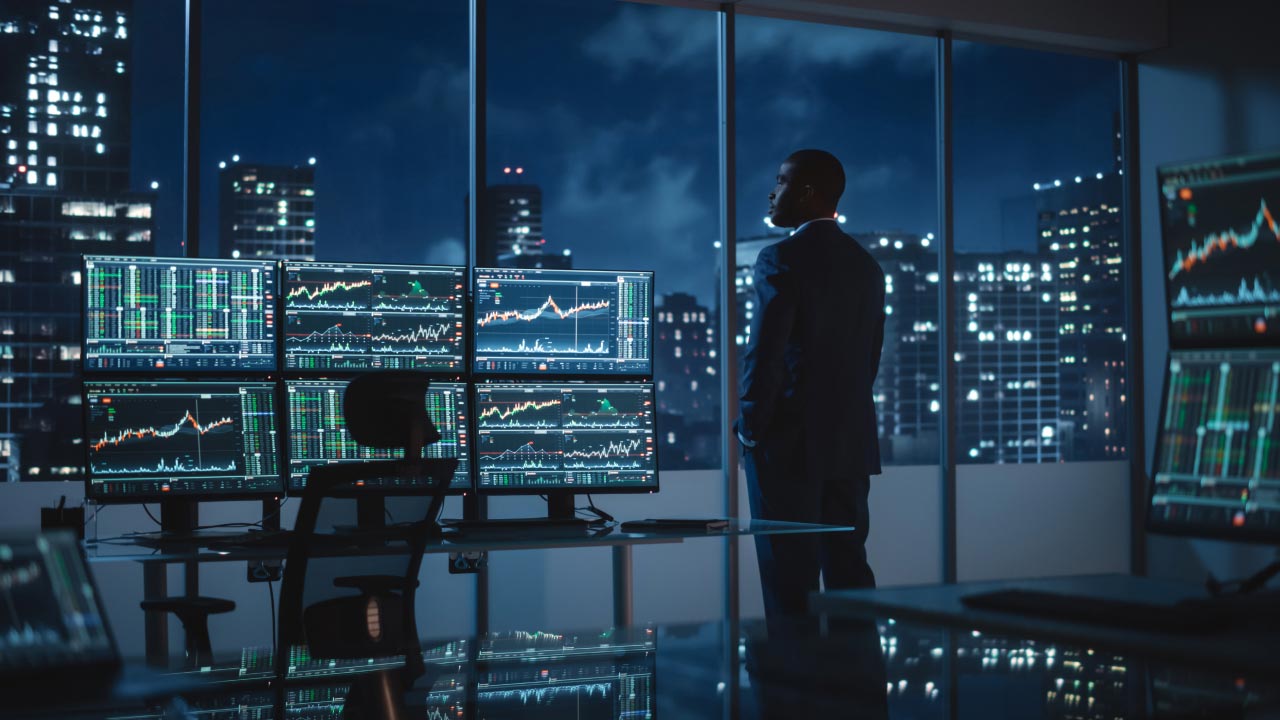 A professional trader stands in a modern office at night, illustrating five questions to ask your forex broker