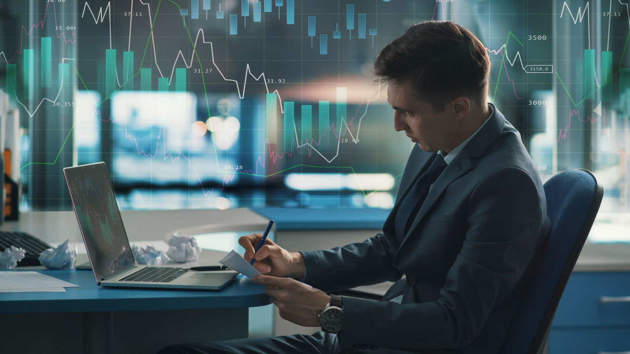 A businessman in a suit analyzing financial documents at his desk with a laptop, illustrating demo accounts, setting goals, and establishing rules