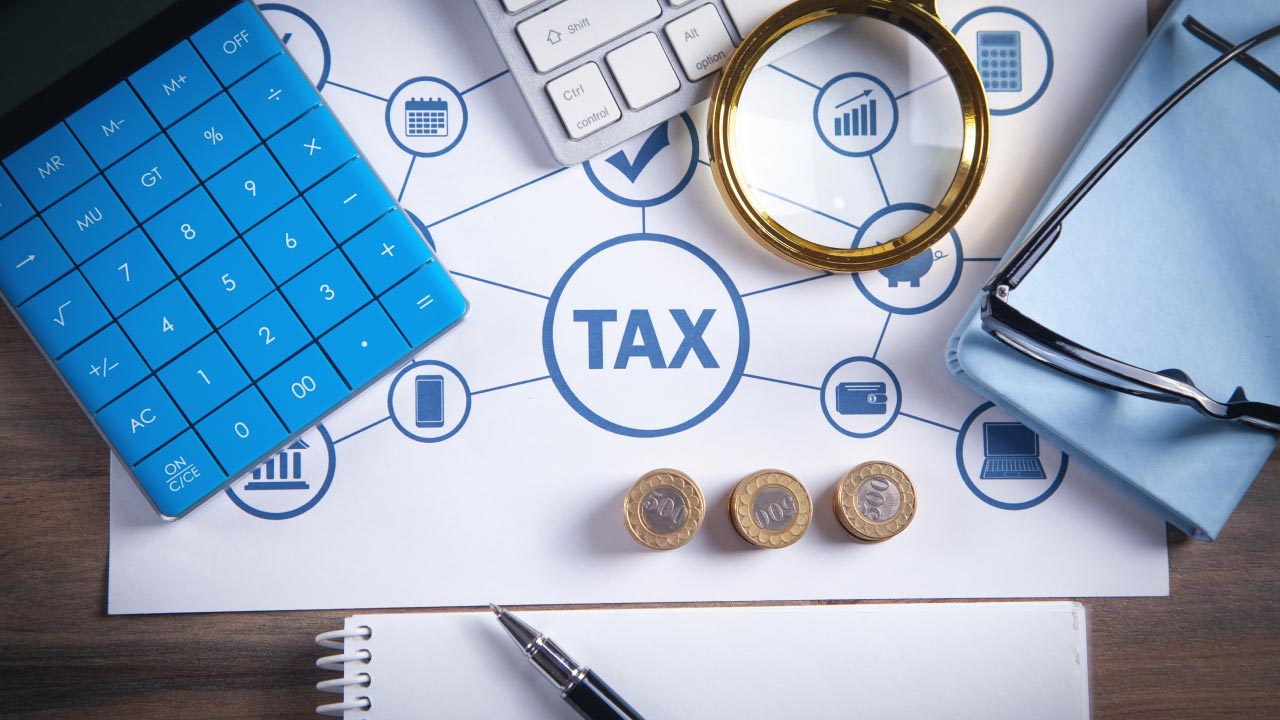 Forex Trading and Taxes: What You Need to Know – Tax-related financial concept with a blue calculator, magnifying glass, coins, notebook, pen, and eyeglasses placed on a paper labeled 'TAX' with financial icons, highlighting tax implications for forex traders.