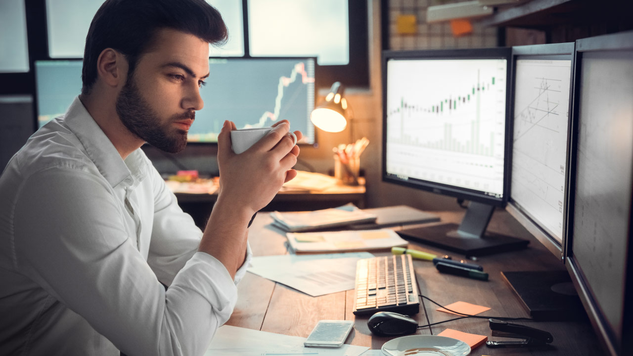 Cryptocurrency Trading Psychology: Everything Traders Should Know – A focused trader analyzing market charts on multiple monitors while holding a cup of coffee, highlighting the importance of discipline and mindset in crypto trading.