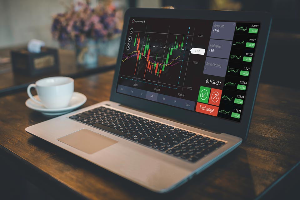 Laptop on a table displaying a trading platform interface with candlestick charts, illustrating the difference between market order and limit order in forex trading.