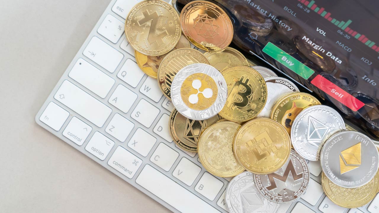 a collection of various physical cryptocurrency coins, including Bitcoin, Ethereum, Ripple, and Litecoin, placed on a white computer keyboard