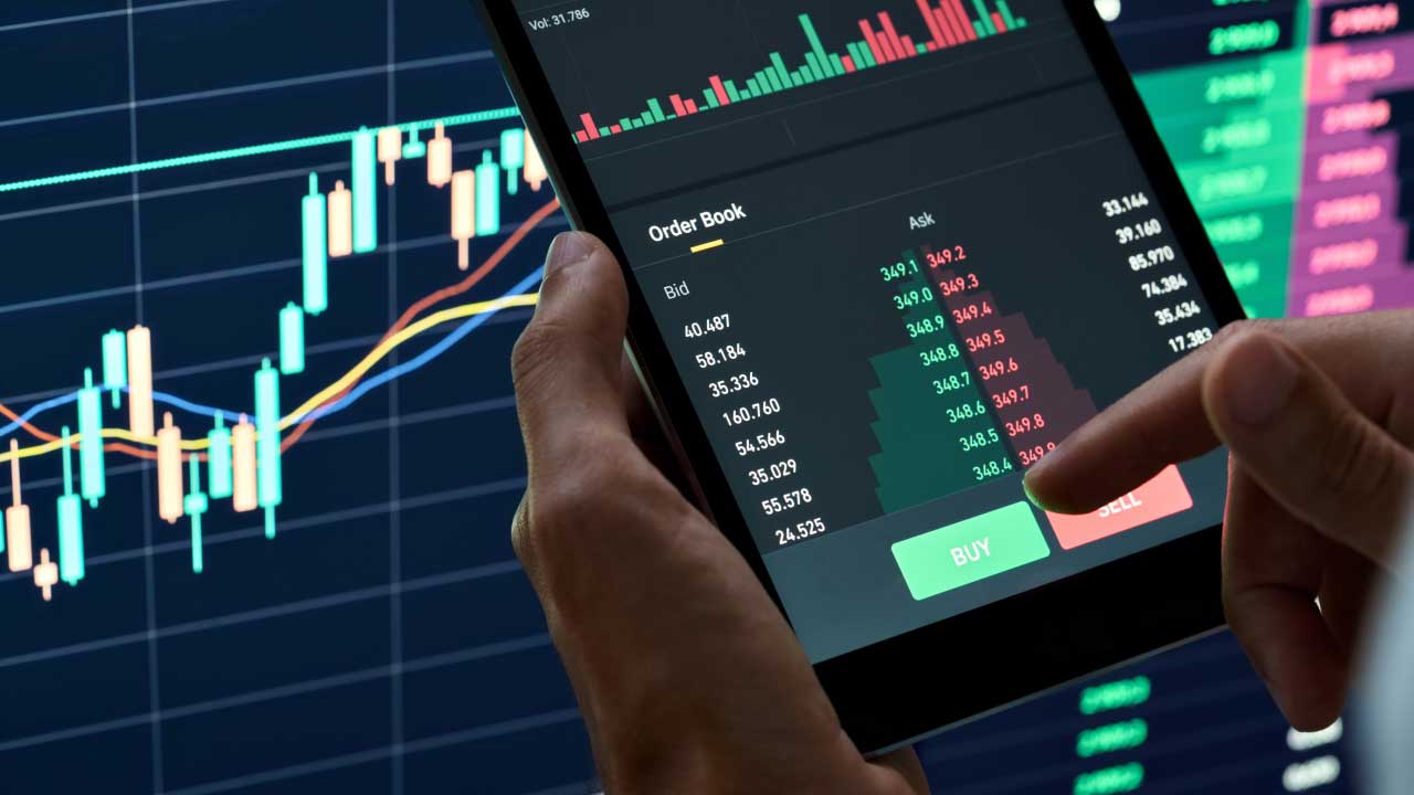 A phone with a hand pointing at the screen, displaying charts and candlesticks, illustrating what the Volatility Index (VIX) is and how to trade it.