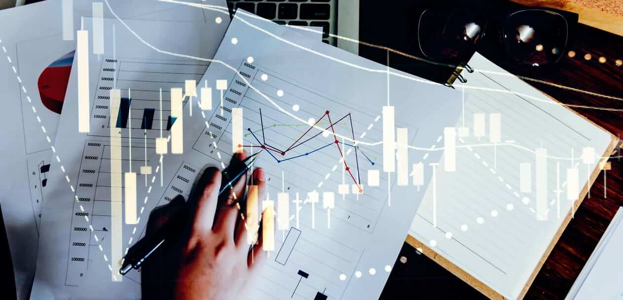 The Basics Of A Fundamental Analysis, illustrated by a hand analyzing printed financial charts with a laptop and notebook nearby, overlaid with candlestick and line chart graphics.