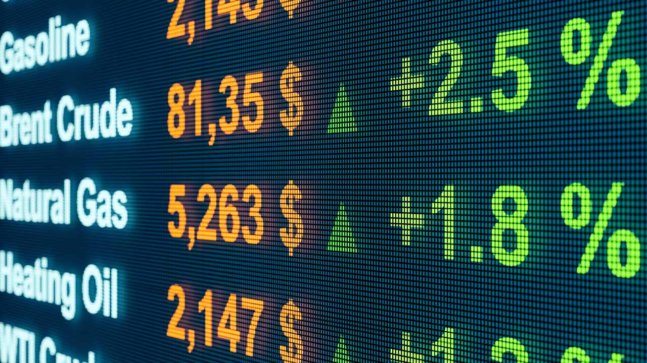 A digital commodities price board displaying rising prices for gasoline, Brent crude, natural gas, heating oil, and WTI crude with green upward arrows and percentage increases.